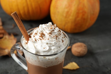 Photo of Pumpkin spice latte with whipped cream and cinnamon stick in glass cup on grey table, closeup