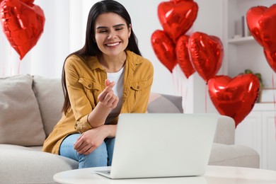 Photo of Valentine's day celebration in long distance relationship. Beautiful young woman showing heart gesture while having video chat with her boyfriend via laptop
