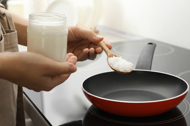 Photo of Woman cooking with coconut oil on induction stove, closeup