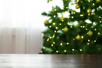 Photo of Blurred view of fir tree with glowing Christmas lights near table indoors