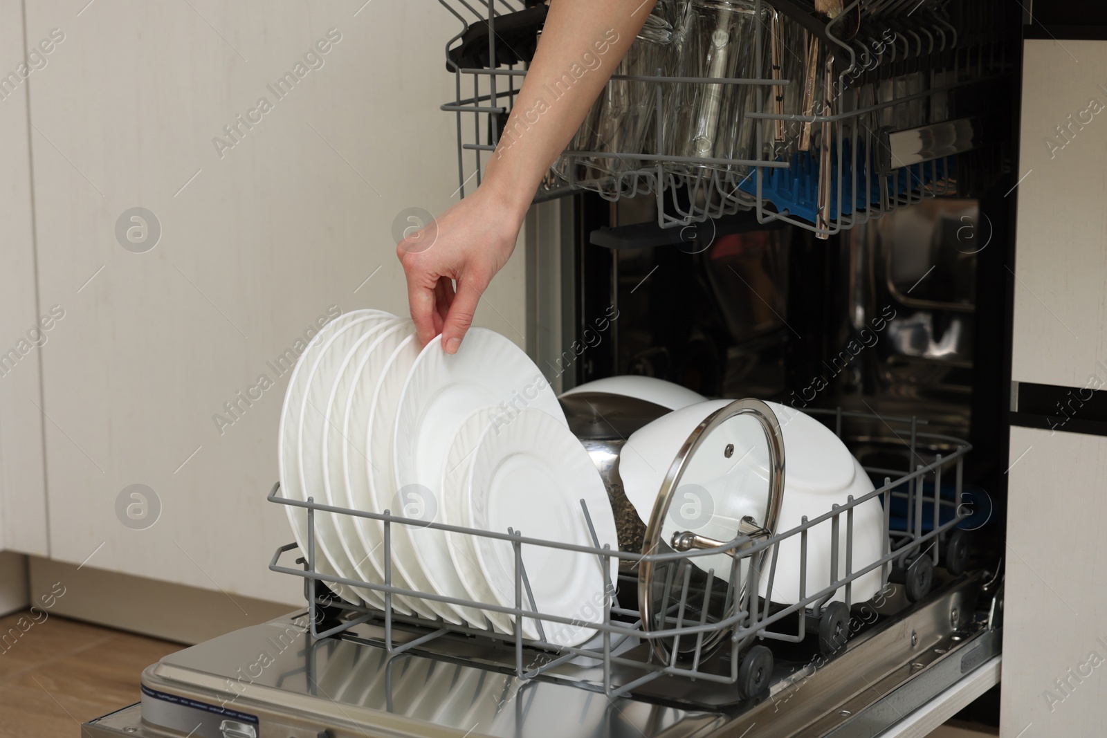 Photo of Woman loading dishwasher with plates indoors, closeup