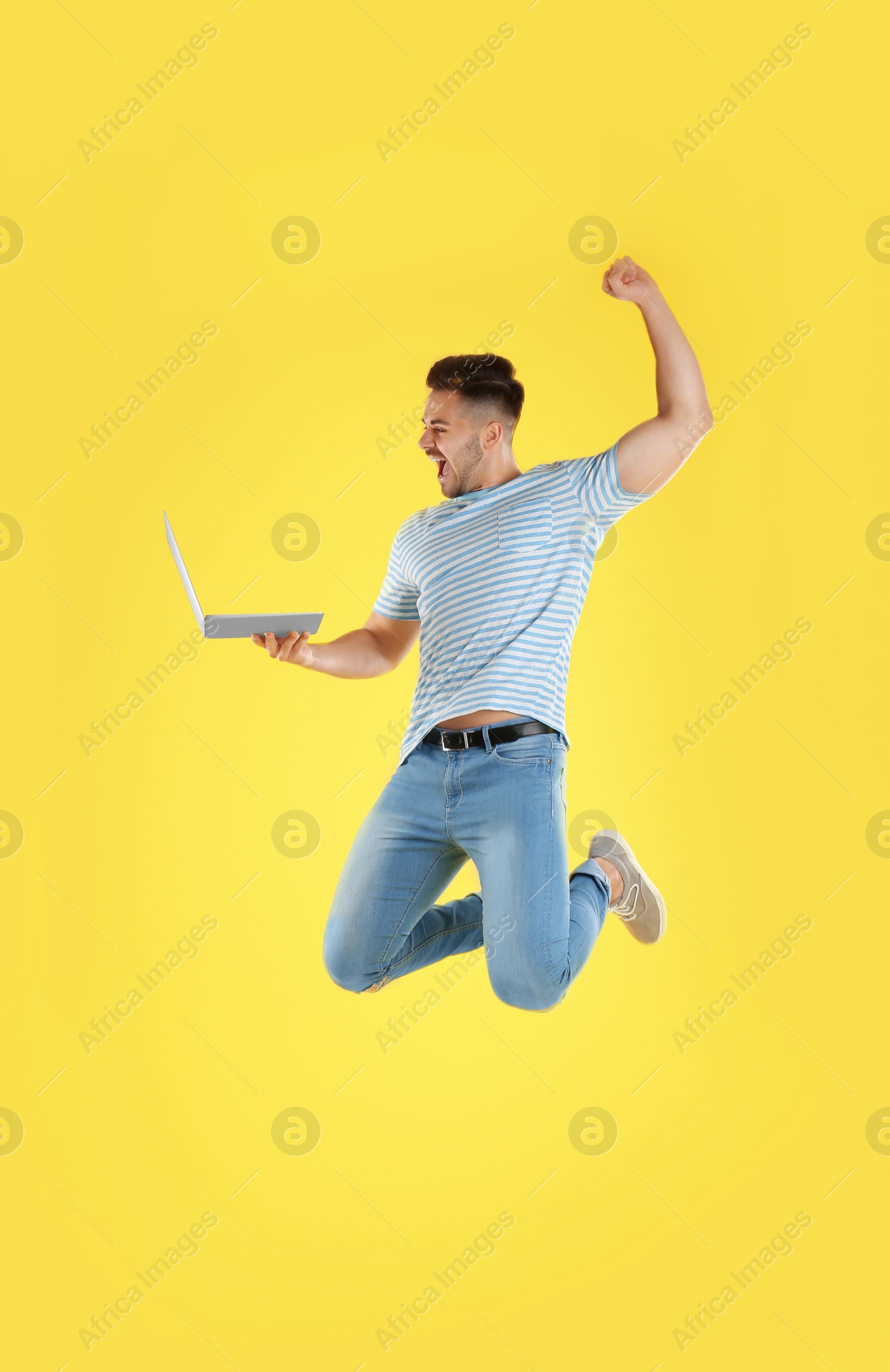 Photo of Emotional man with laptop jumping on yellow background