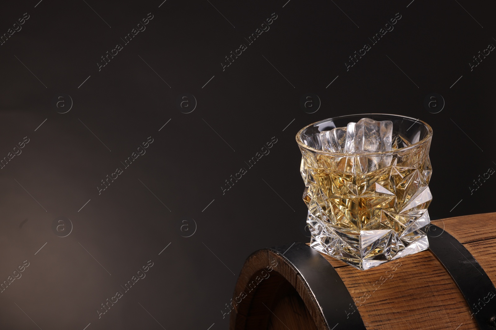 Photo of Whiskey in glass on wooden barrel against dark background, space for text