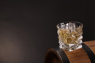 Whiskey in glass on wooden barrel against dark background, space for text