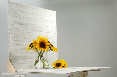 Photo of Glass vase with beautiful sunflowers and double-sided backdrop on table in photo studio