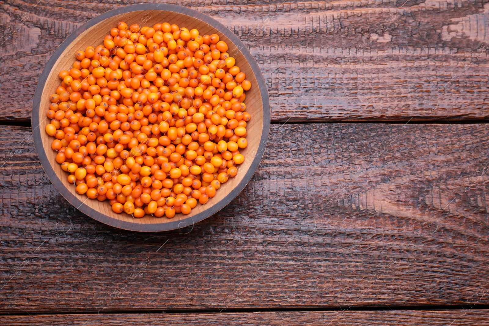 Photo of Bowl with fresh ripe sea buckthorn berries on wooden table, top view. Space for text