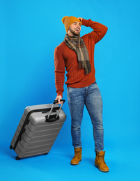 Photo of Young man in warm clothes with suitcase on blue background. Winter vacation