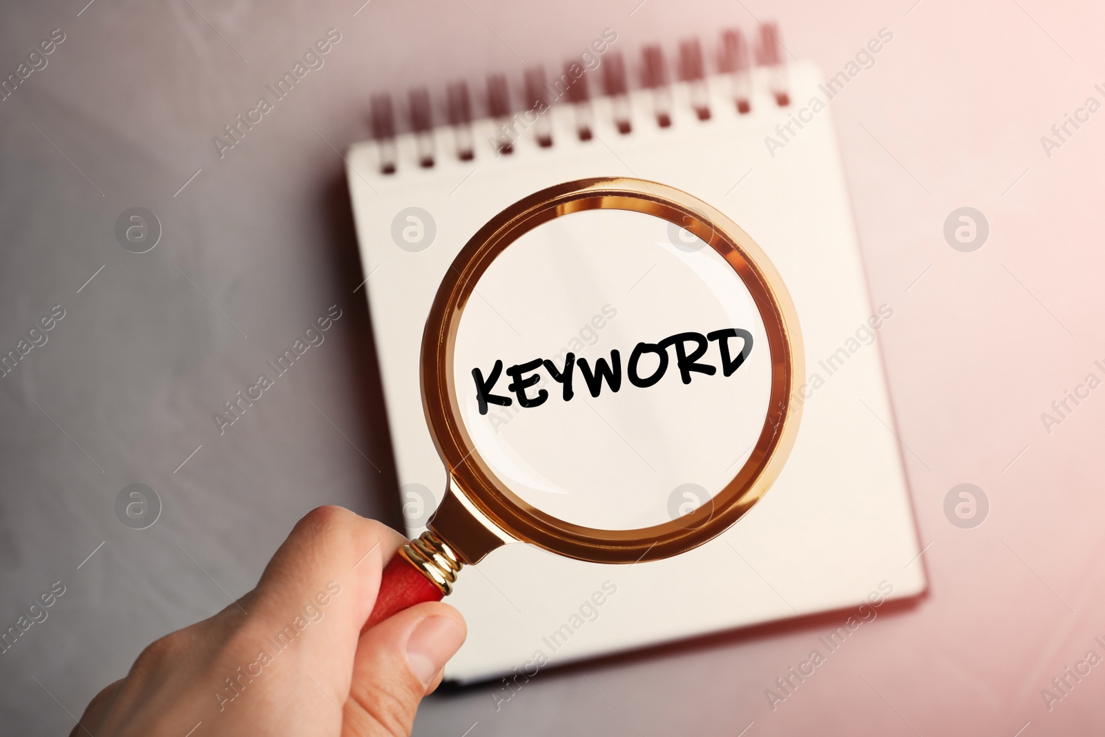 Image of Woman looking at word Keyword written in notebook through magnifying glass, closeup