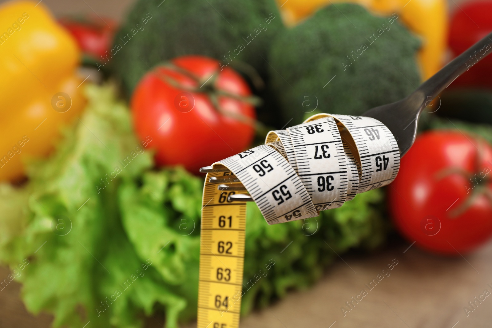 Photo of Fork with measuring tape and blurred vegetables on background, space for text. Weight loss