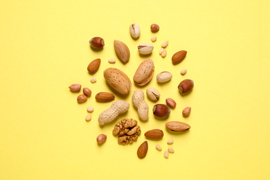 Different delicious nuts on yellow background, flat lay