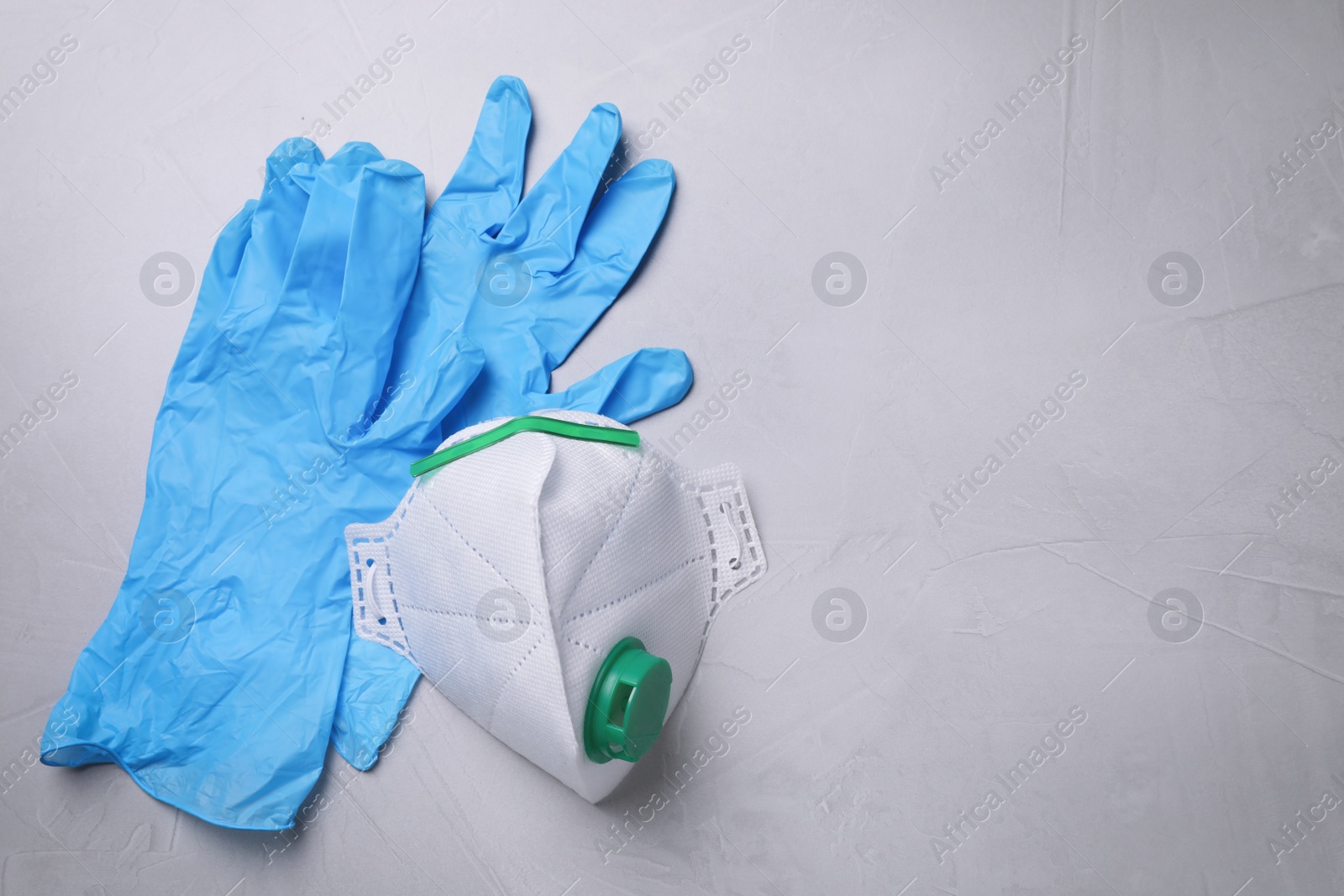 Photo of Protective medical gloves and respirator on light grey stone background, flat lay with space for text