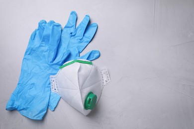 Photo of Protective medical gloves and respirator on light grey stone background, flat lay with space for text