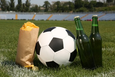 Photo of Football ball with beer and chips on green field grass in stadium