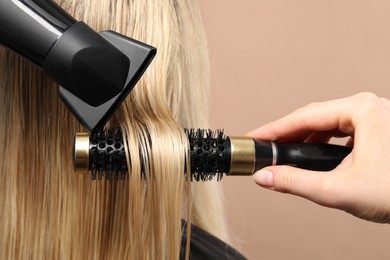 Hairdresser blow drying client's hair on beige background, closeup