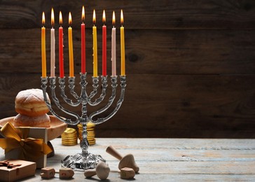 Photo of Hanukkah celebration. Menorah with burning candles, dreidels, donuts and gift boxes on wooden table, space for text