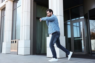 Photo of Emotional man talking on smartphone and looking at watch while running from building. Being late concept