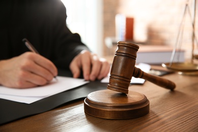 Photo of Judge working at table in office, focus on gavel. Law and justice concept