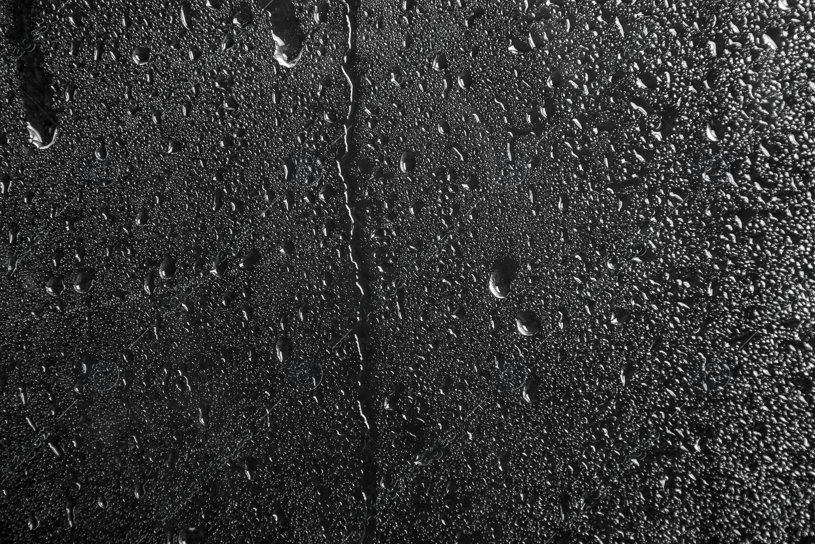 Photo of Glass with rain drops against dark background