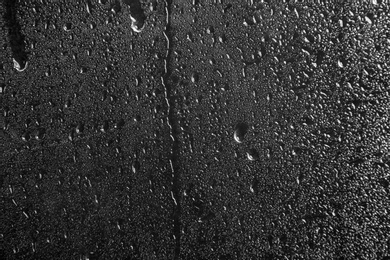 Photo of Glass with rain drops against dark background