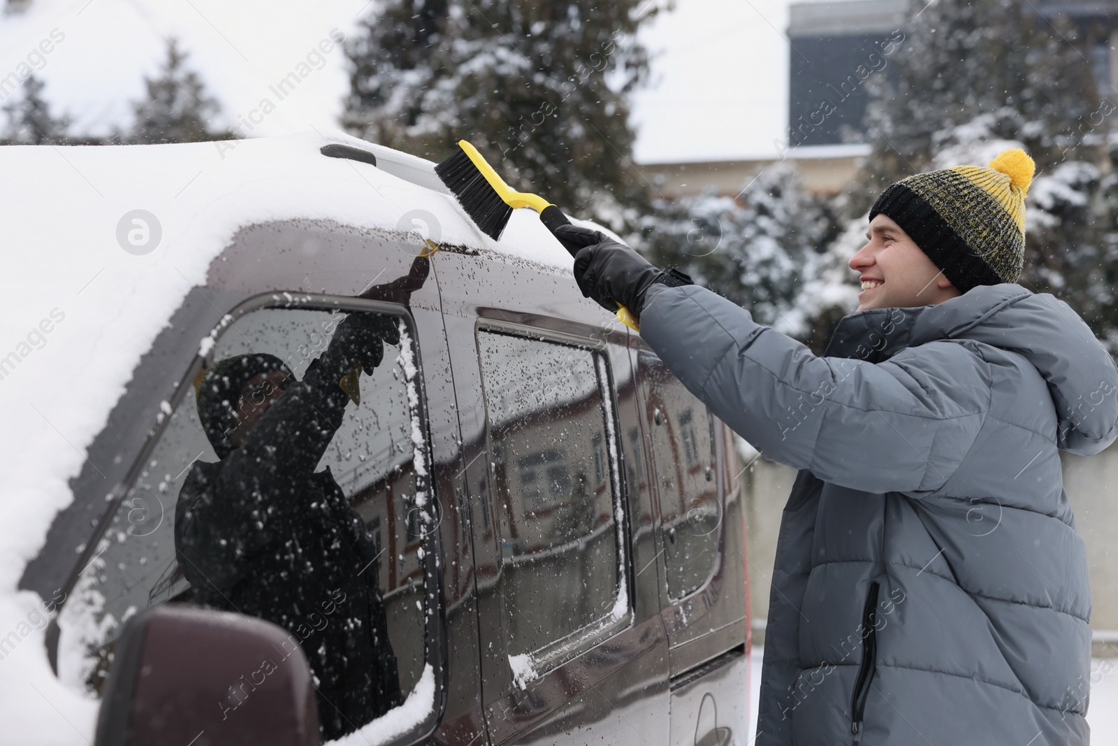 Photo of Man cleaning snow from car with brush outdoors