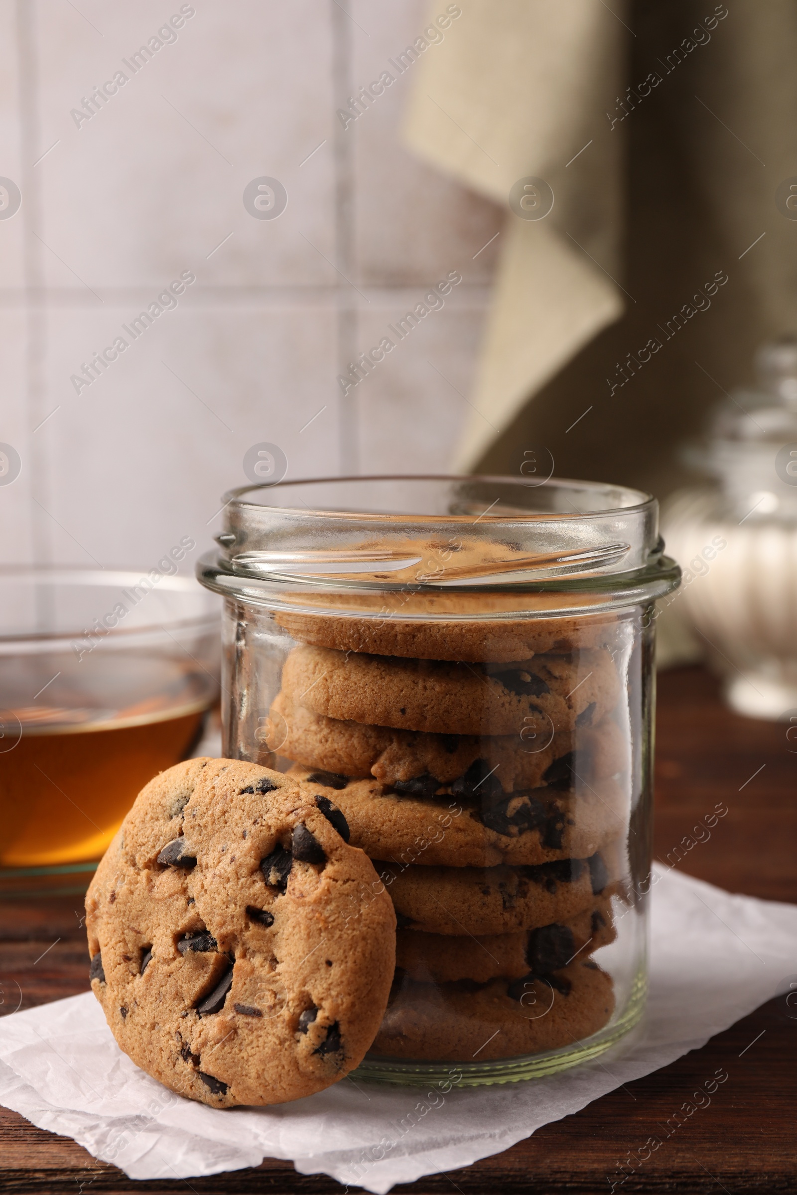 Photo of Glass jar with delicious chocolate chip cookies and tea on wooden table