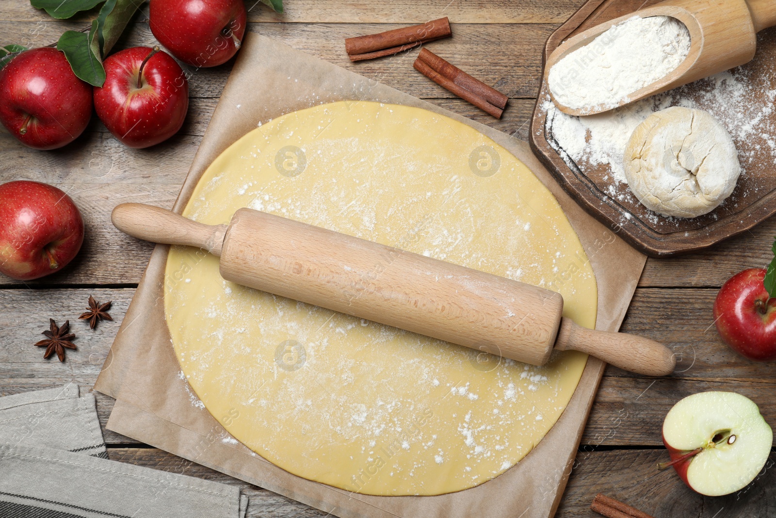 Photo of Dough for apple pie and ingredients on wooden table, flat lay