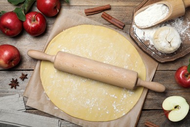 Photo of Dough for apple pie and ingredients on wooden table, flat lay