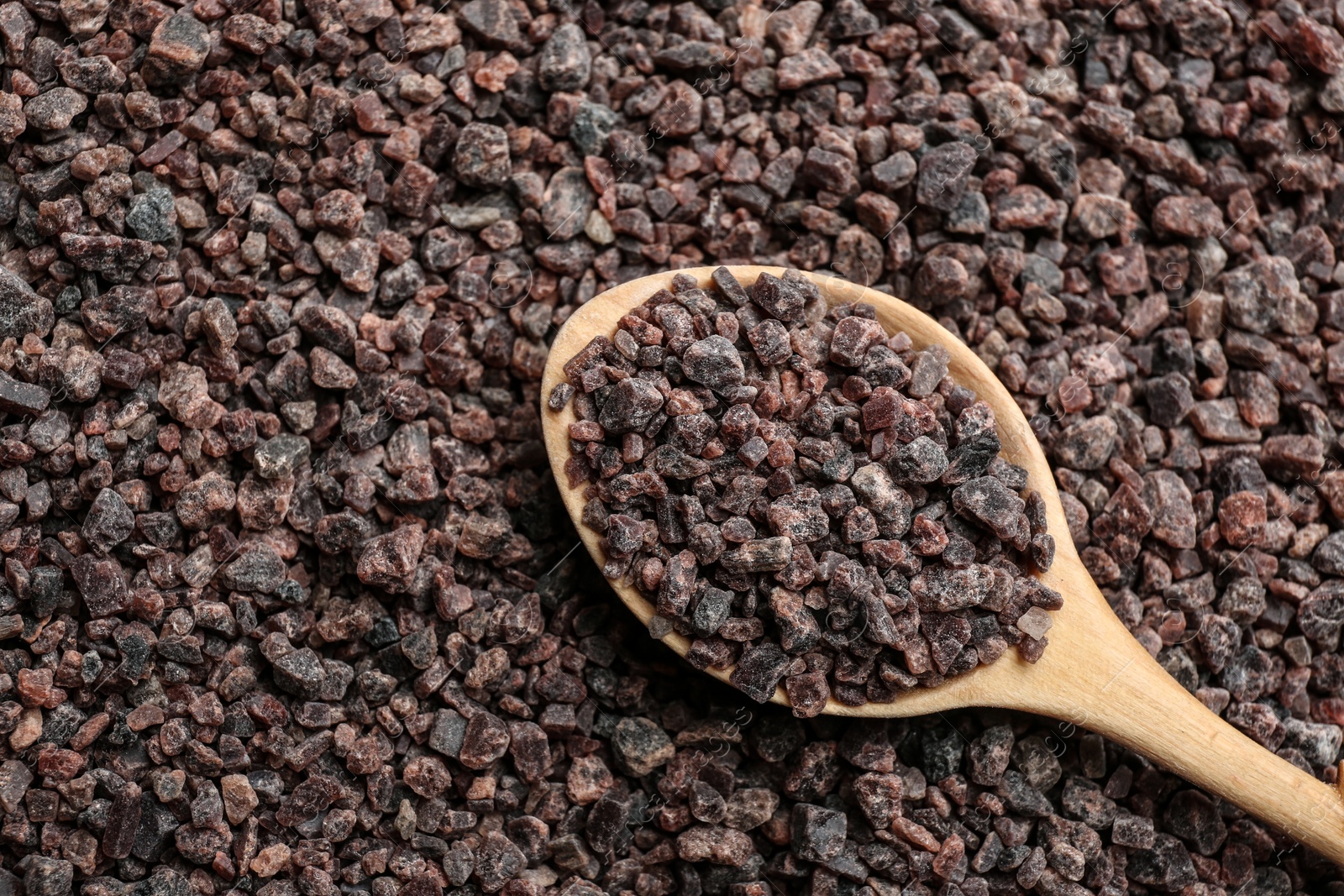 Photo of Pile of black salt with wooden spoon, top view