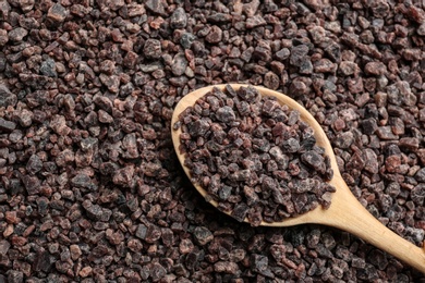 Photo of Pile of black salt with wooden spoon, top view