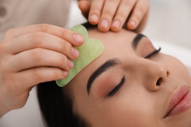 Photo of Young woman receiving facial massage with gua sha tool in beauty salon, closeup