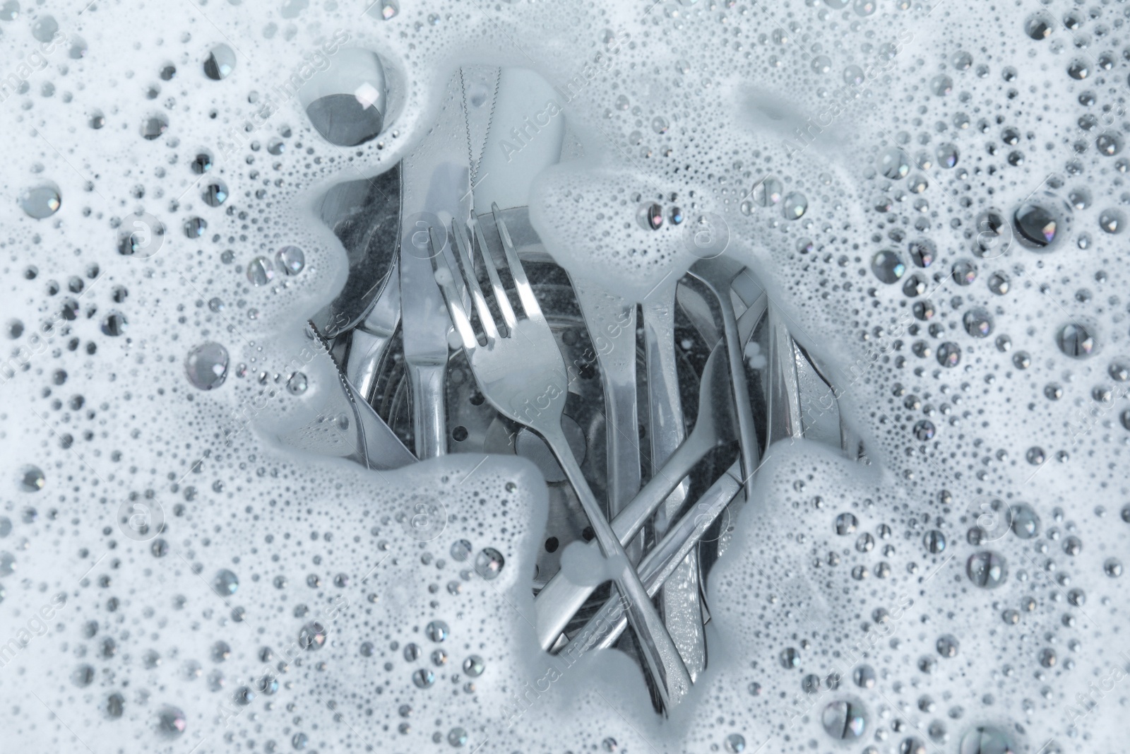 Photo of Washing silver spoons, forks and knives in water with foam, flat lay