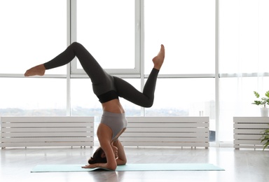 Photo of Young woman practicing headstand with splits in yoga studio