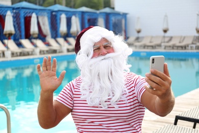 Authentic Santa Claus taking selfie near swimming pool outdoors