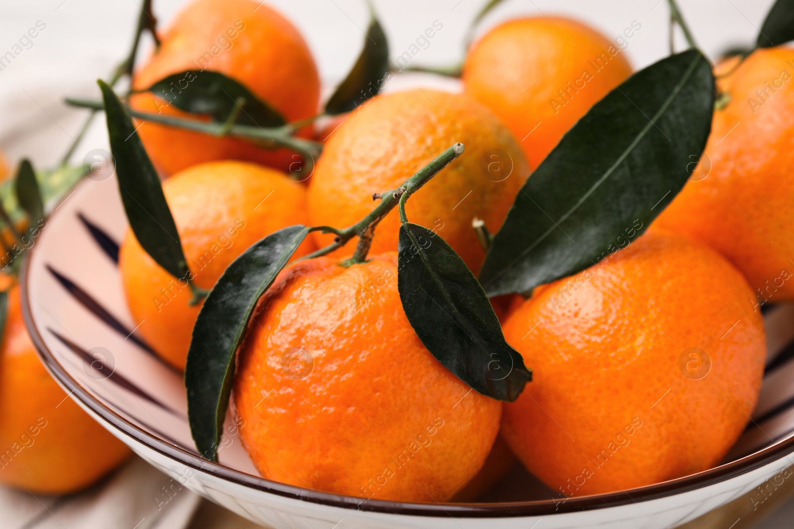 Photo of Fresh ripe tangerines with green leaves in bowl on table, closeup