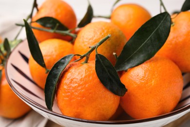 Fresh ripe tangerines with green leaves in bowl on table, closeup