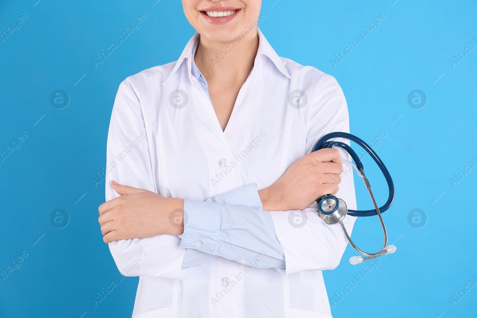 Photo of Young doctor with stethoscope on blue background, closeup