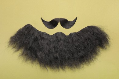 Artificial moustache and beard on khaki background, top view