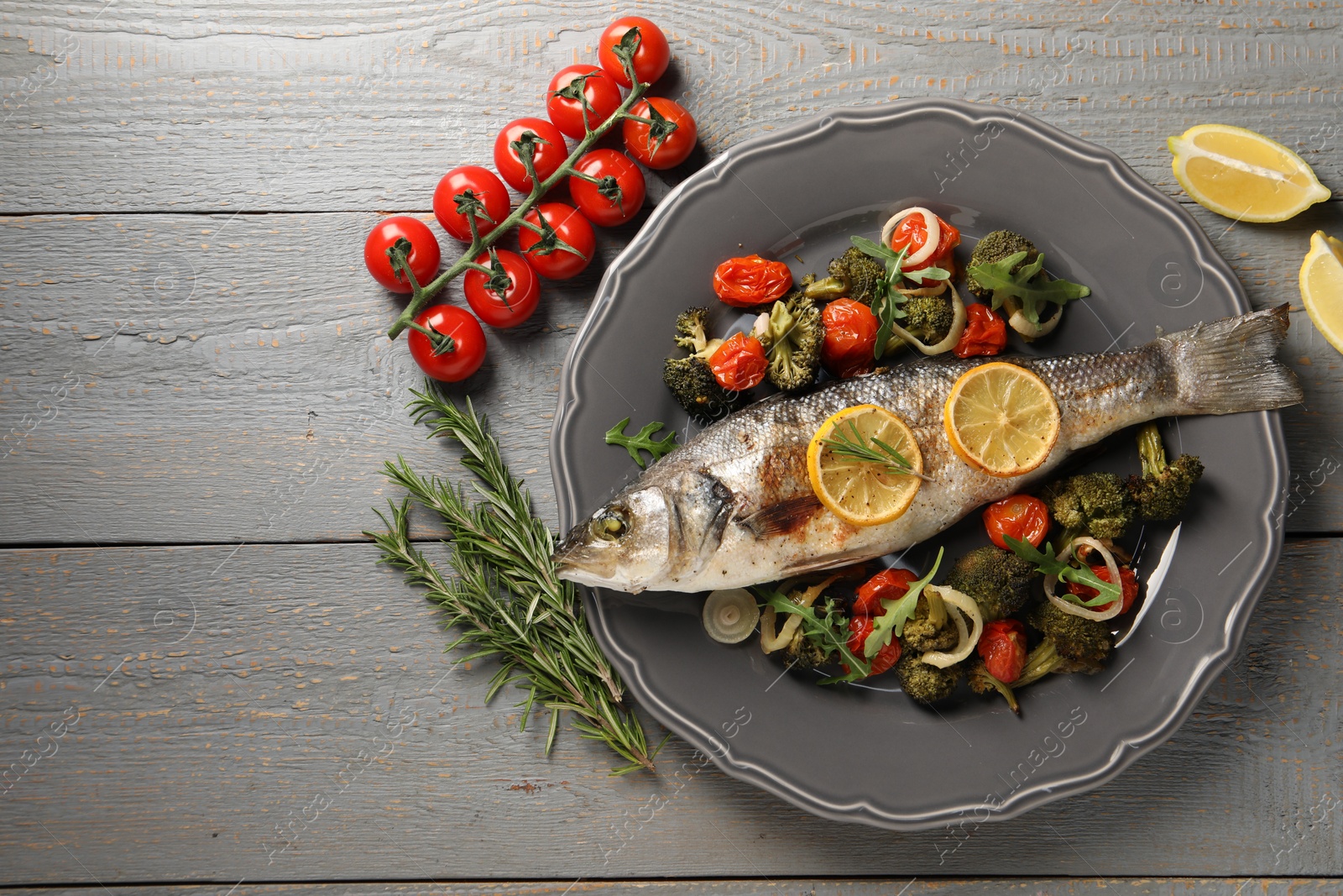 Photo of Baked fish with vegetables, rosemary and lemon on grey wooden table, flat lay. Space for text