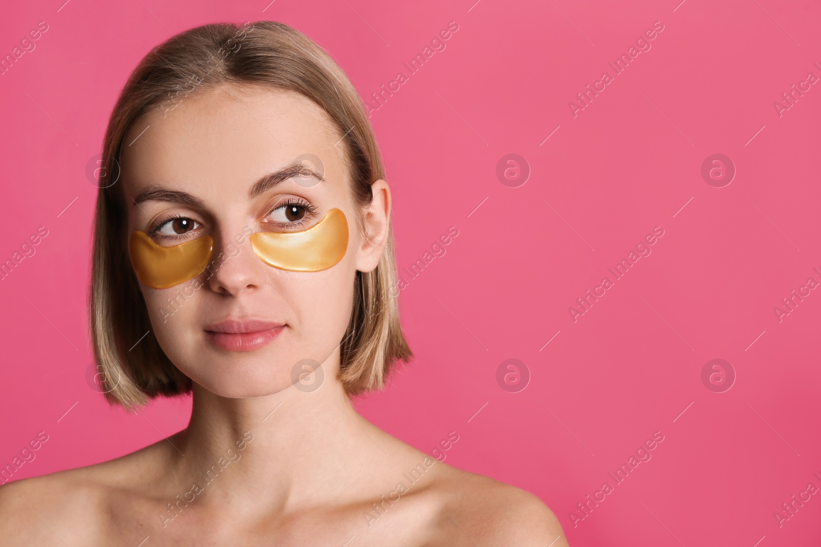 Photo of Beautiful young woman with under eye patches on pink background, space for text