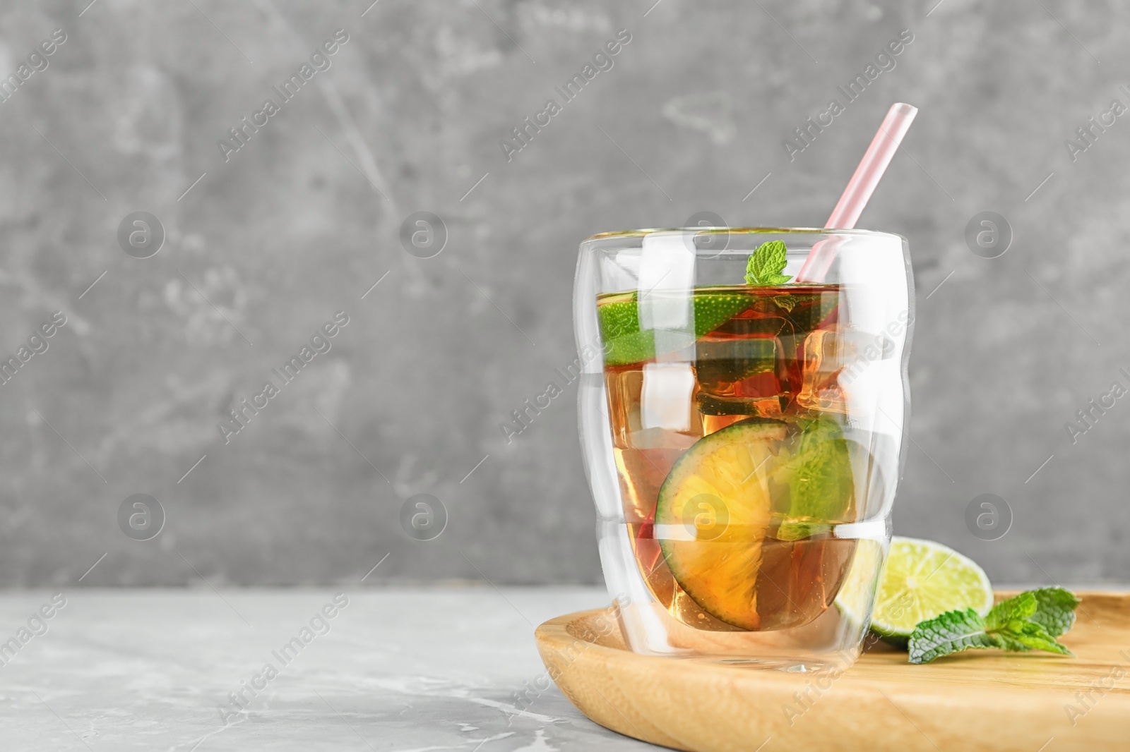 Photo of Glass of refreshing iced tea on marble table against grey background. Space for text