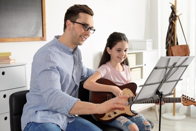 Little girl playing guitar with her teacher at music lesson. Learning notes