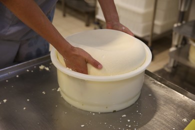 Photo of Worker taking fresh cheese from mould at modern factory, closeup