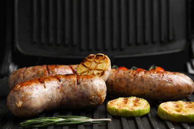 Cooking delicious fresh sausages with vegetables on modern grill
