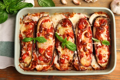 Photo of Baked eggplant with tomatoes, cheese and basil in dishware on wooden table, flat lay