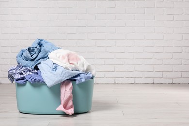 Laundry basket with clothes near white brick wall. Space for text