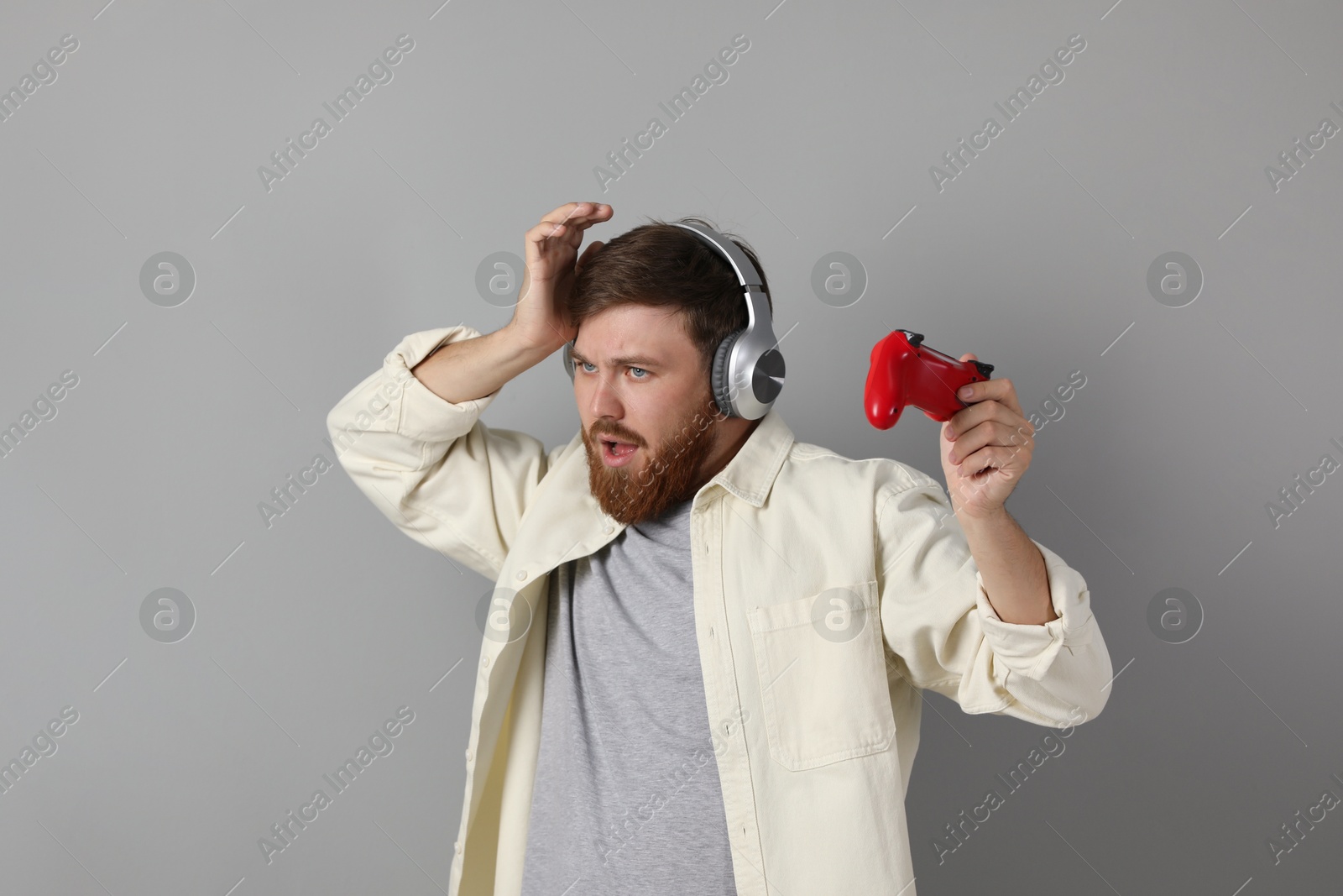 Photo of Confused man in headphones with game controller on grey background