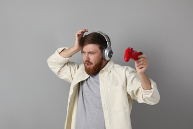 Confused man in headphones with game controller on grey background