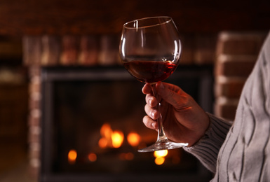 Man with glass of wine near fireplace at home, closeup