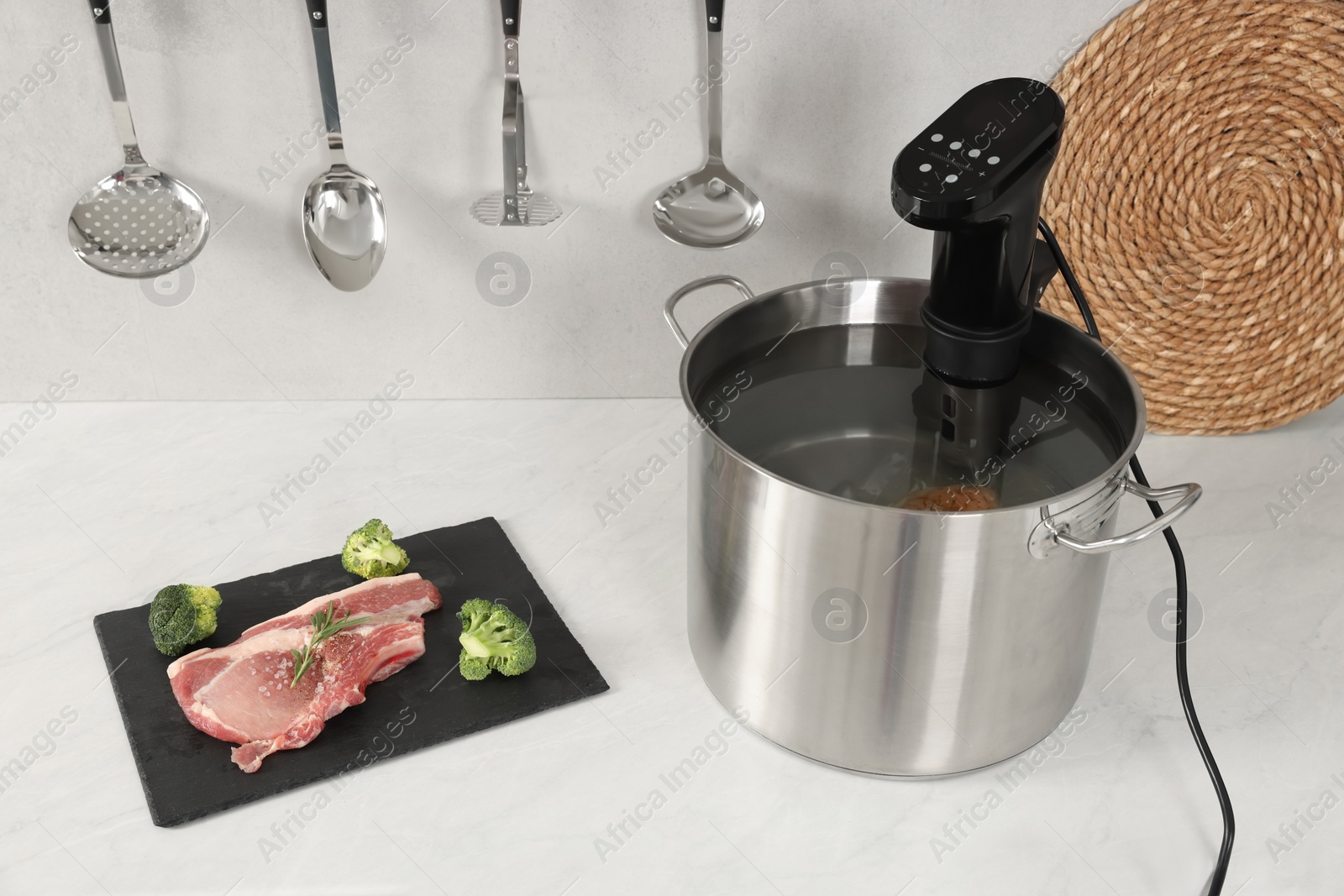 Photo of Pot with sous vide cooker and ingredients on table in kitchen. Thermal immersion circulator