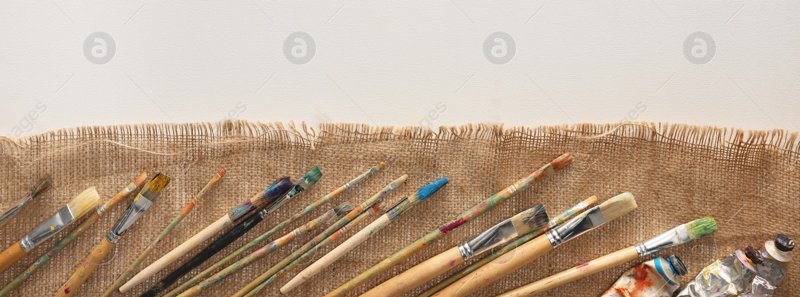 Photo of Natural burlap fabric and different painting supplies on white background, top view. Space for text